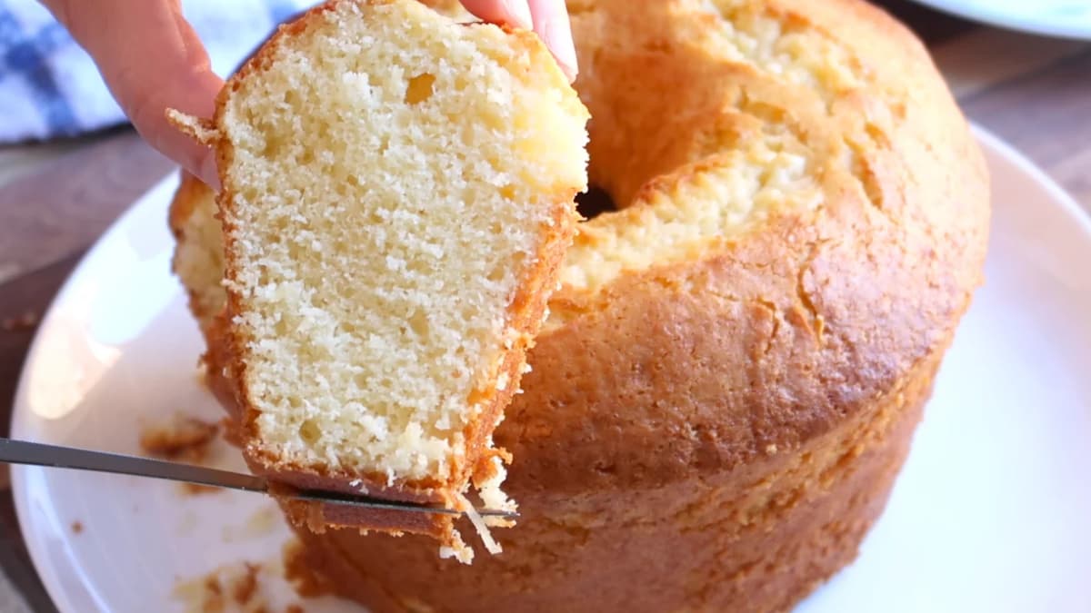 Fatia de bolo de queijo ralado diante do bolo dourado com furo no meio